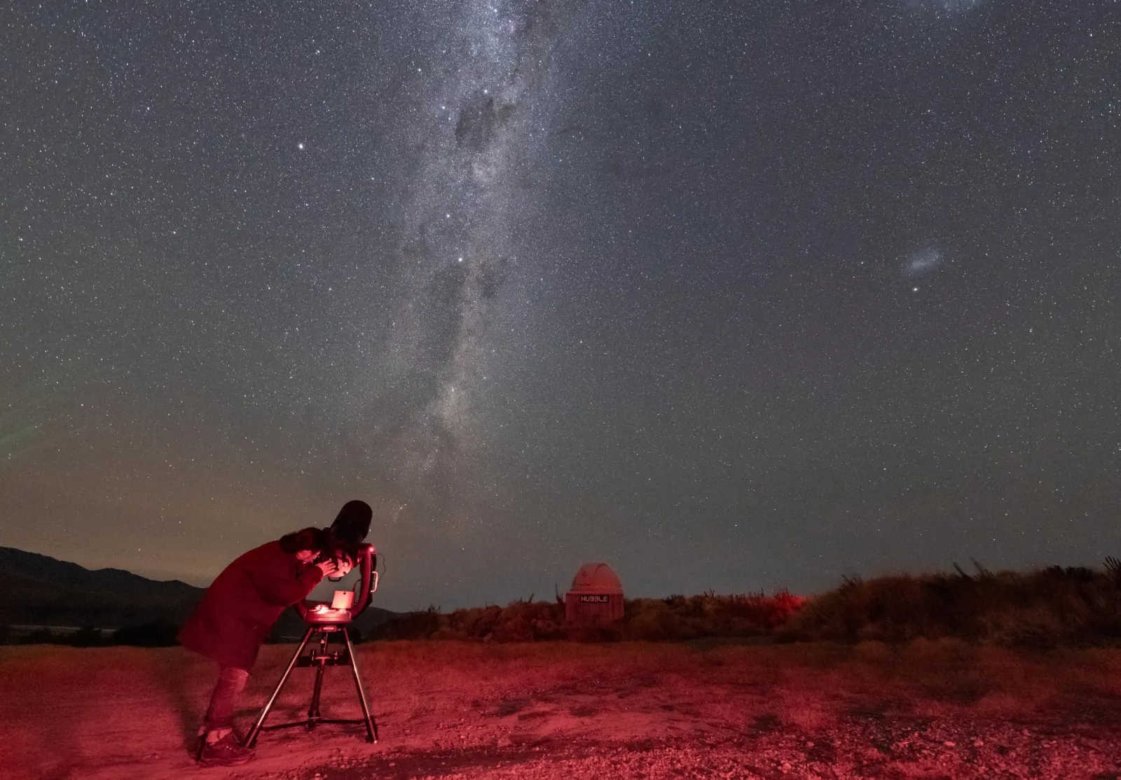 Guide adjusting a telescope under the Milky Way in the crater