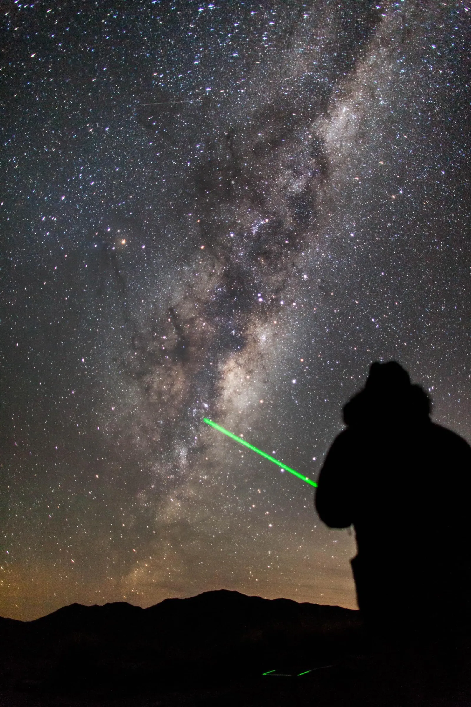 Silhouetted guide pointing a laser at the Milky Way core