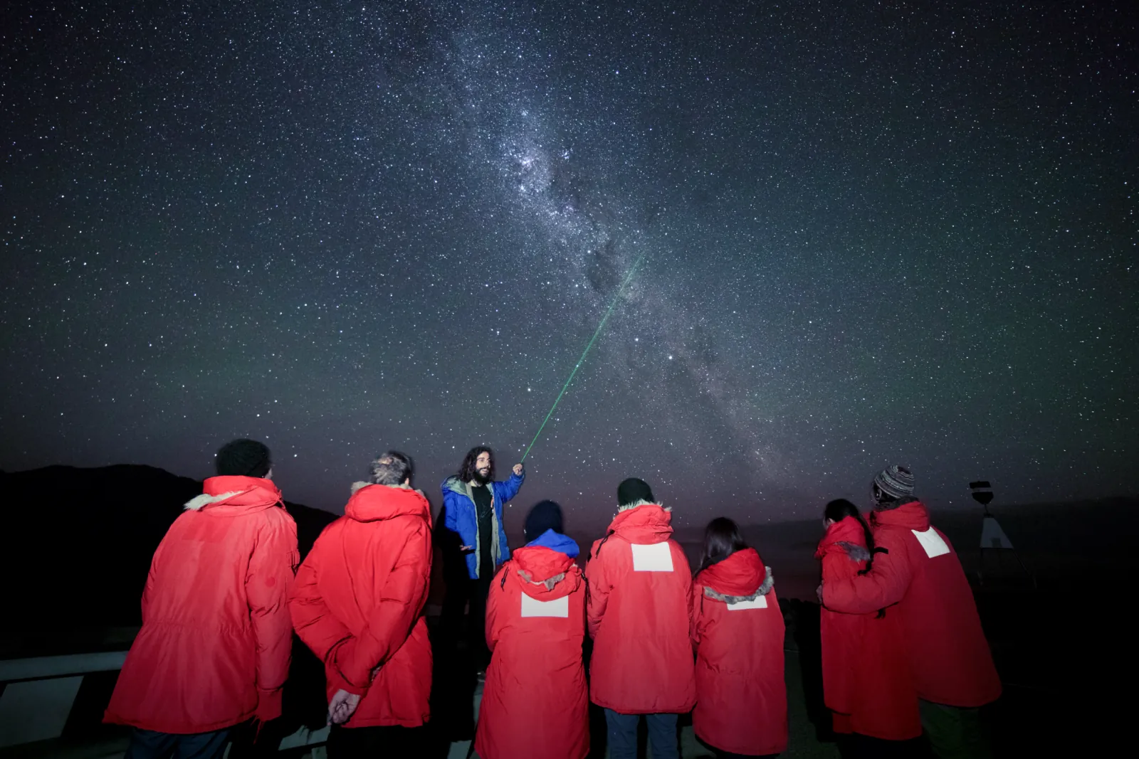 Guests in red cold-weather jackets on the Mount John summit under the Milky Way