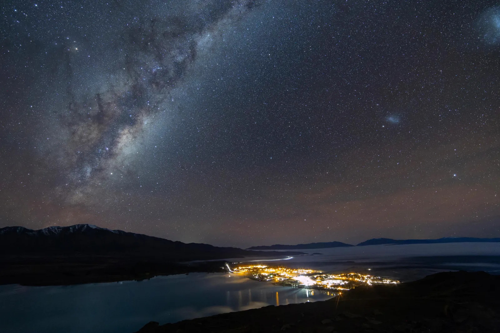 Milky Way above the lights of Lake Tekapo village seen from Mount John