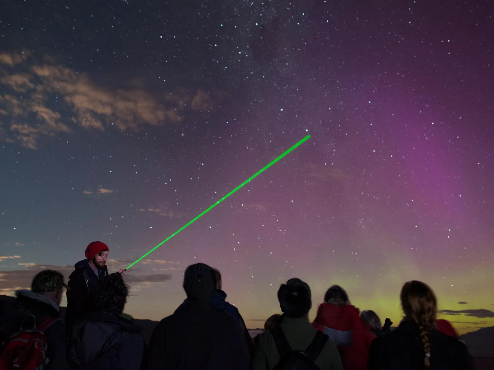 Green laser pointing to stars above guests on the Mount John summit