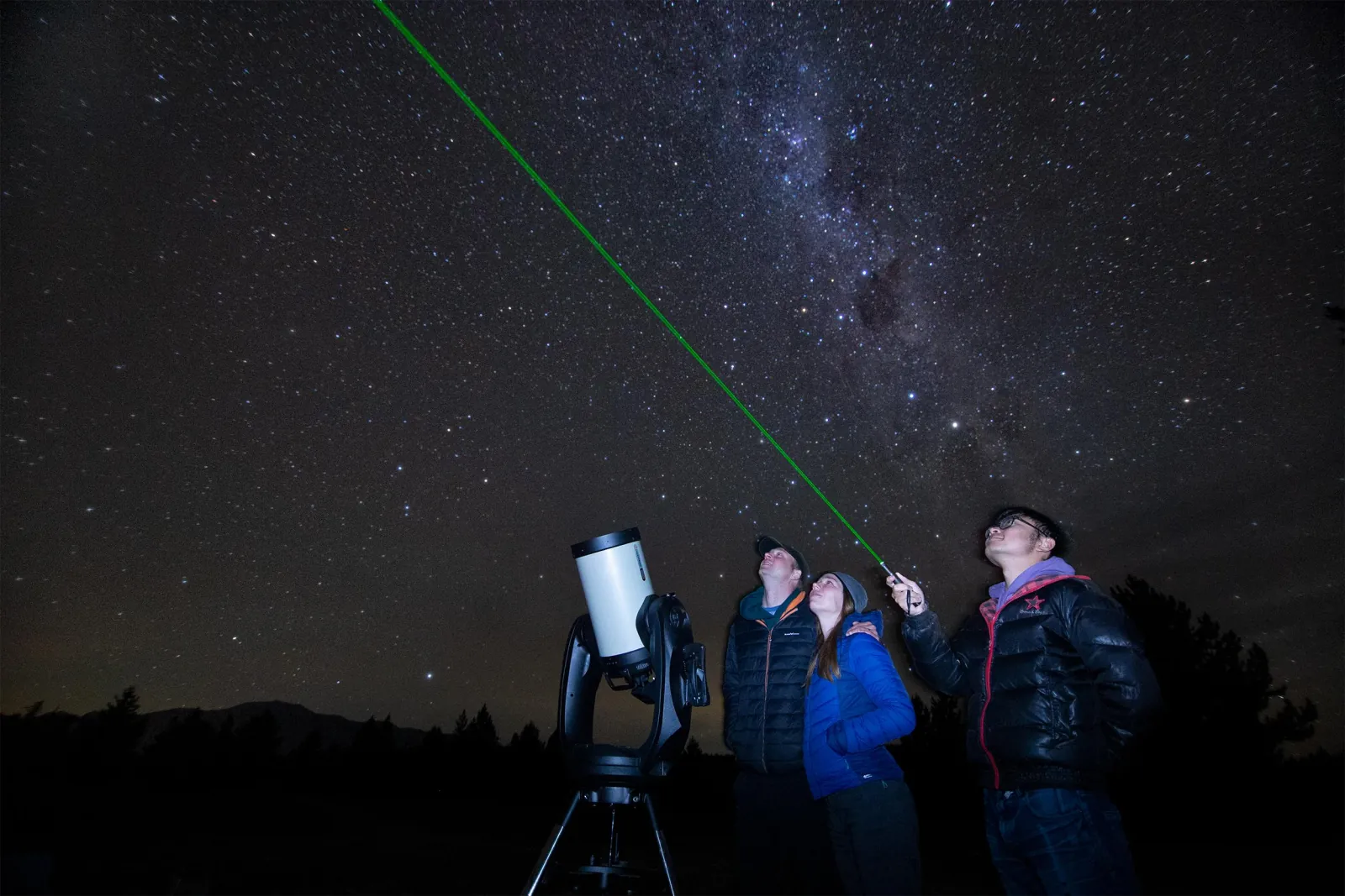 Guide's green laser pointing out stars to a small group beside the telescope