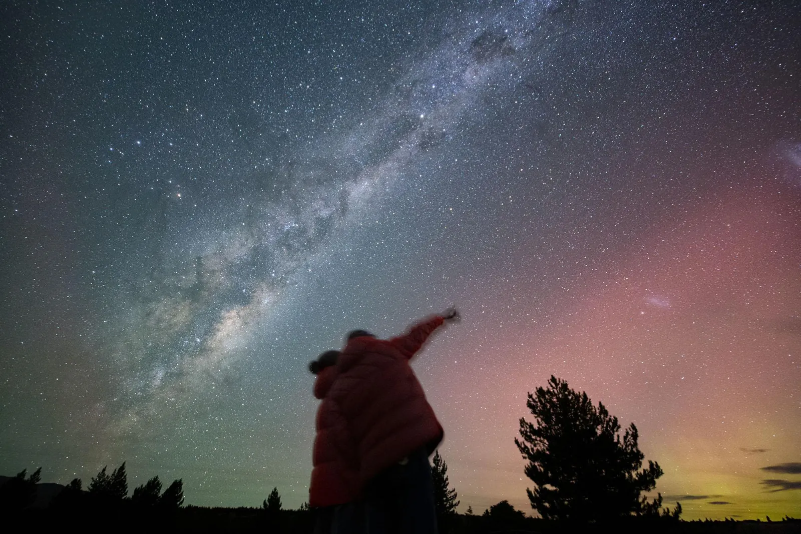 Guest pointing up at the Milky Way core above the trees at Lake Tekapo