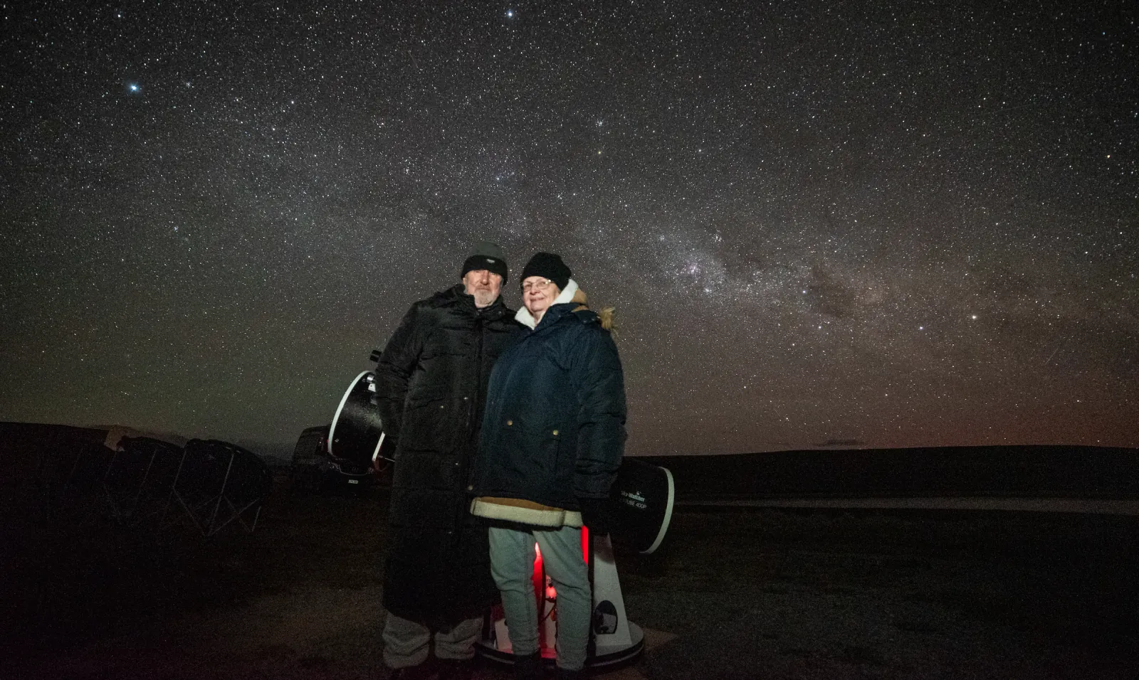 Couple in down jackets beside the 16-inch telescope at night