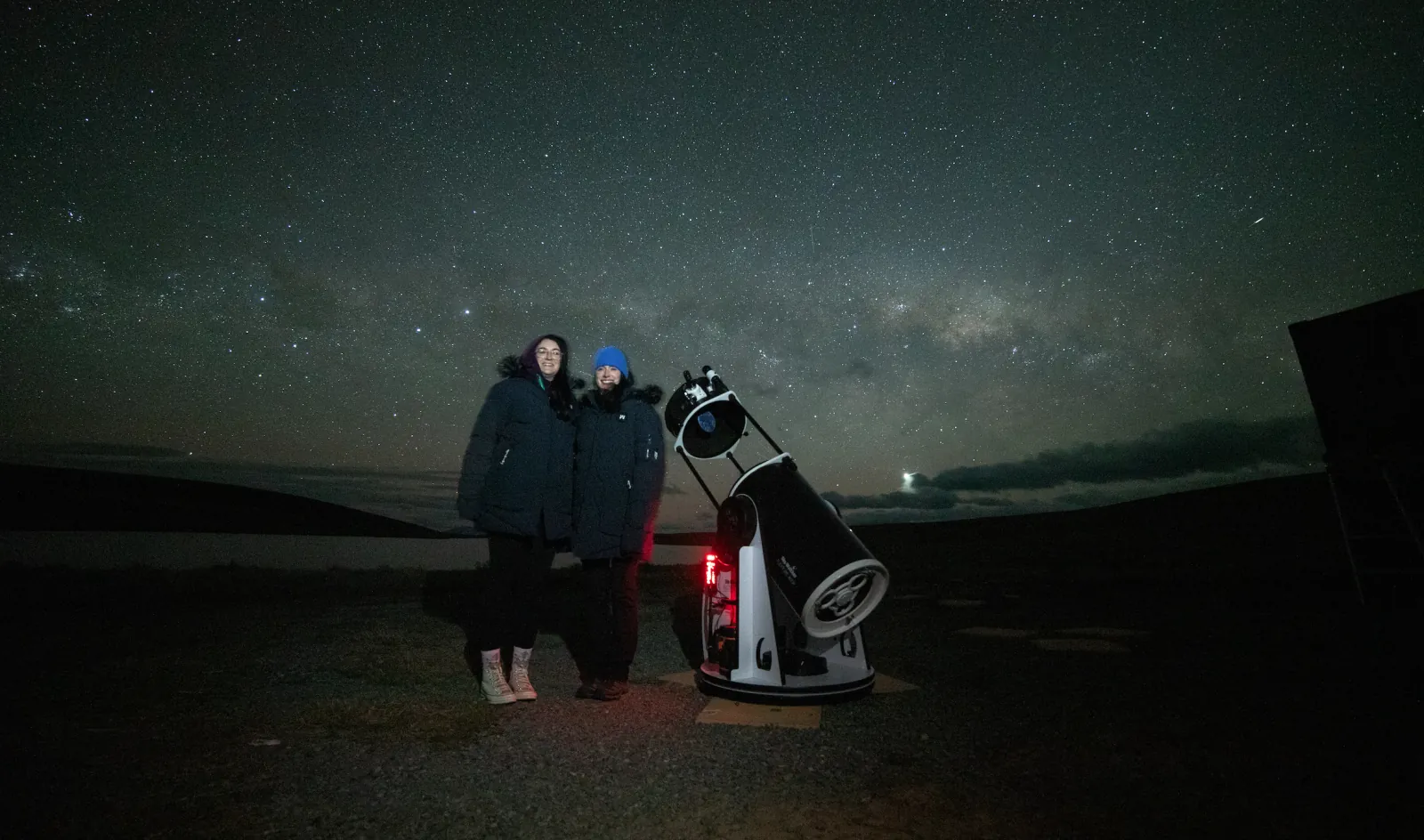 Guests standing by the telescope with the Milky Way above the farm